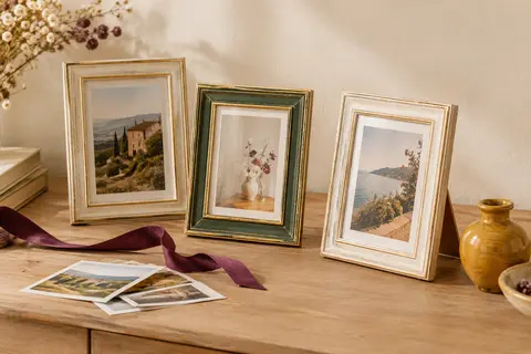 Trois cadres photo vintage Afuly, un vert et deux blancs avec accents dorés, posés sur une console claire.