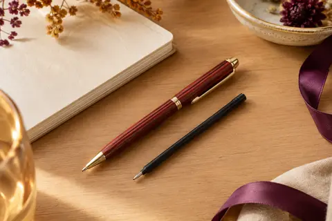 Stylo bille rouge à l’aspect bois et recharge noire posés sur un bureau clair avec un carnet
