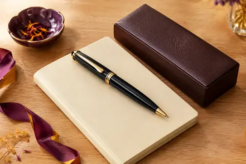 Stylo roller noir laqué aux finitions dorées posé sur un carnet crème près de sa boîte de présentation.