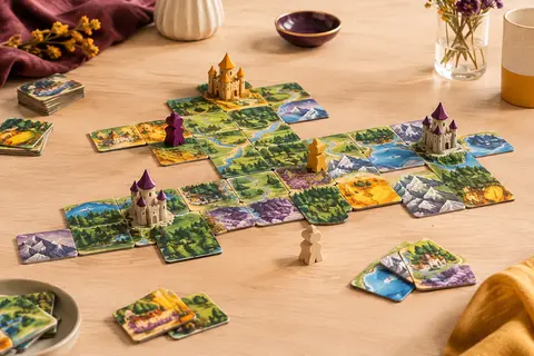 Dominos de paysages, châteaux en trois dimensions et rois en bois sur une table claire.