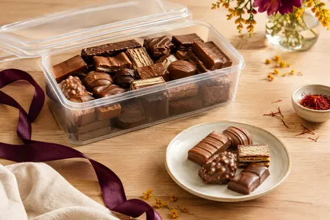 Boîte refermable de chocolats assortis présentée ouverte sur une table en bois clair