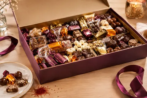 Coffret ouvert de mini chocolats assortis emballés individuellement, présenté sur une table en bois clair.
