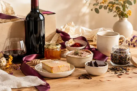 Coffret gourmand avec vin rouge, foie gras, terrine, miel, chocolat et thé sur une table claire