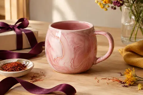 Mug en céramique rose marbré avec poignée, présenté sur une table en bois clair.