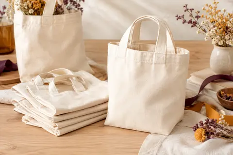 Lot de sacs en coton naturel écru à anses courtes, présentés sur un fond de bois clair.