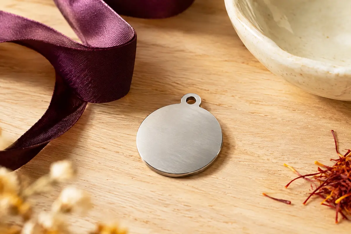 Médaille ronde argentée pour animal posée sur du bois clair avec un ruban prune et une coupelle en céramique