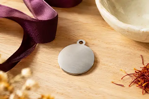 Médaille ronde argentée pour animal posée sur du bois clair avec un ruban prune et une coupelle en céramique