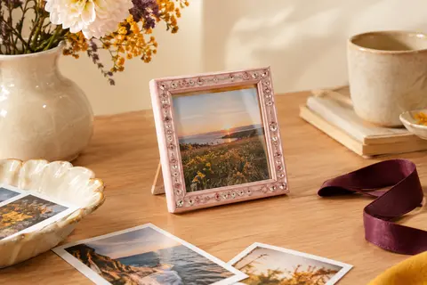 Cadre photo carré rose clair scintillant posé sur une table en bois clair, avec une photo en son centre.