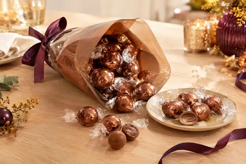 Cornet de bouchées LINDOR au chocolat au lait présenté avec quelques chocolats sur une assiette en céramique