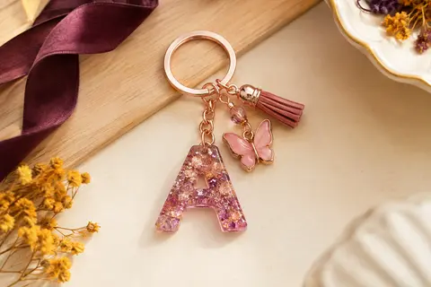 Porte-clés à initiale en résine pailletée, avec pendentif papillon rose, anneau métallique et pampille.