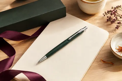 Stylo bille Parker Jotter XL vert mat posé sur un carnet crème, près de son coffret cadeau
