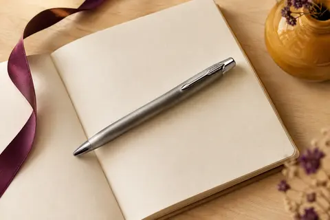 Stylo-bille Parker Urban métallique brossé posé sur un carnet crème avec des détails décoratifs prune et safran