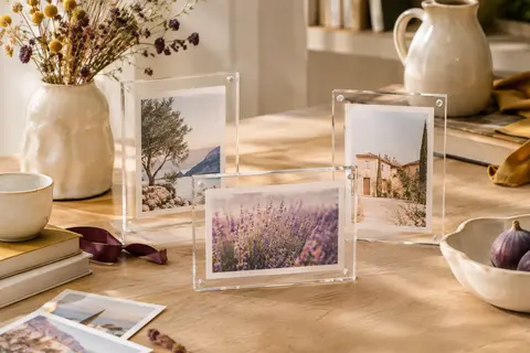 Lot de cadres photo transparents en acrylique posés sur une table en bois clair avec des images de souvenirs.