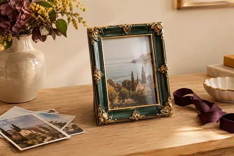 Cadre photo baroque vert et or posé sur une console en bois clair, avec une photo au format 10 x 15 cm.