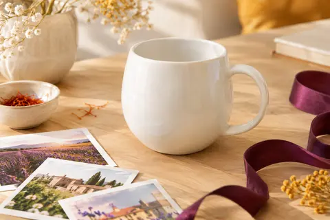 Mug personnalisable en porcelaine brillante posé sur une table en bois clair avec des photos