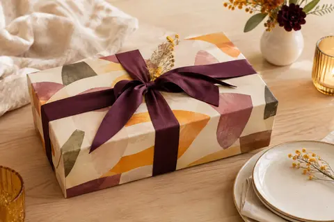 Coffret cadeau rectangulaire multicolore présenté sur du bois clair avec un ruban prune et une touche de céramique