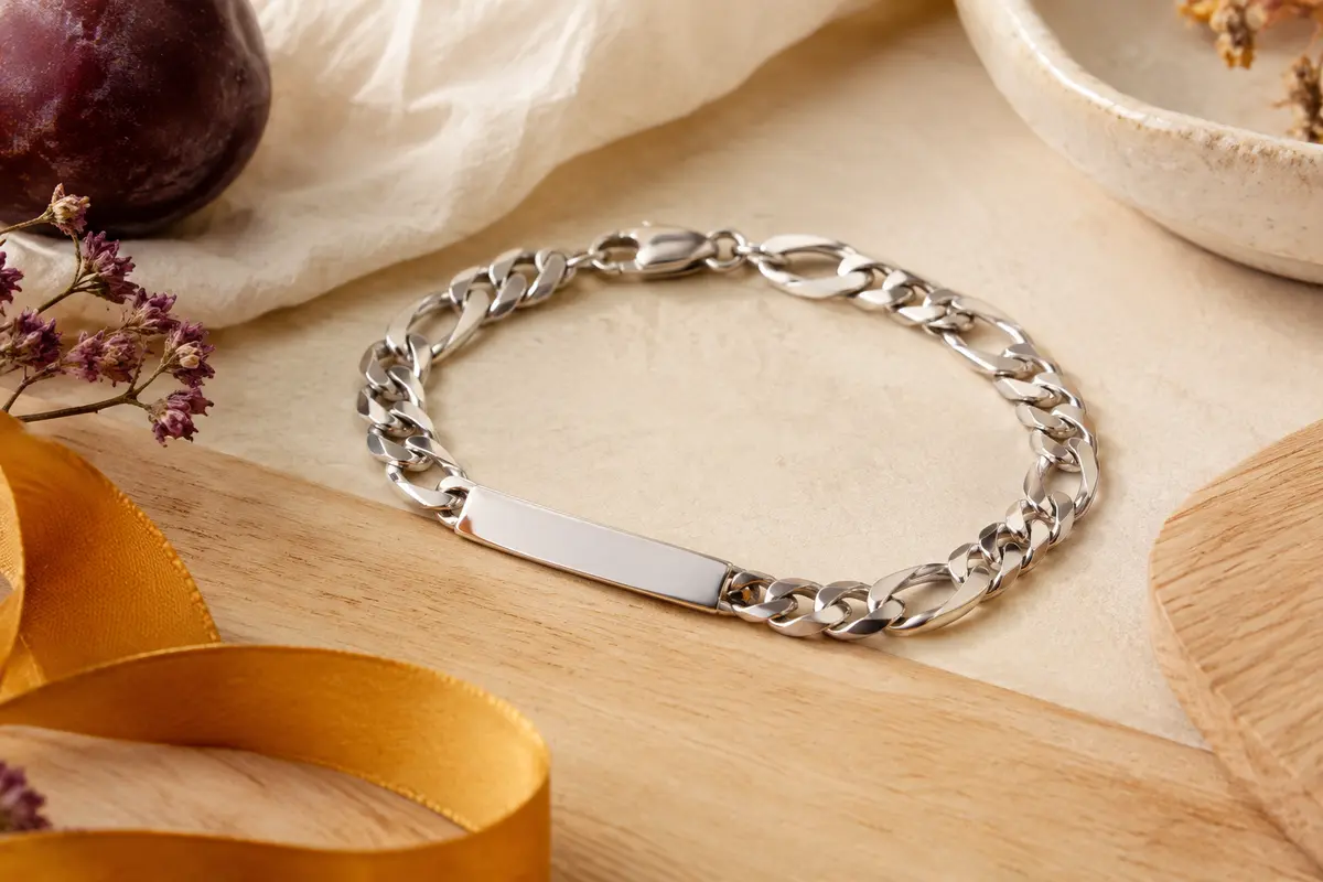 Bracelet gourmette Figaro argenté avec fermoir mousqueton, posé sur un fond crème et bois clair