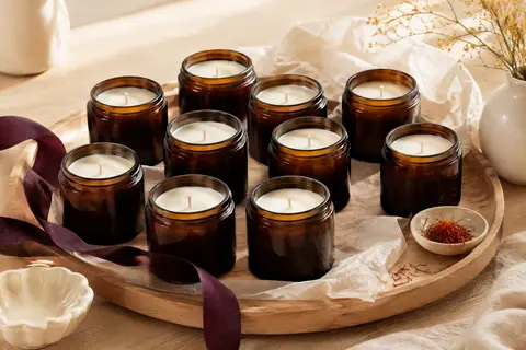Dix bougies parfumées en bocaux de verre marron disposées sur un plateau en bois clair.