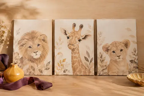 Trois affiches en toile beige aux motifs de lion et de girafe, présentées sans cadre sur du bois clair.